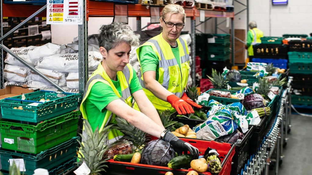Two women sorting food into crates in a warehouse