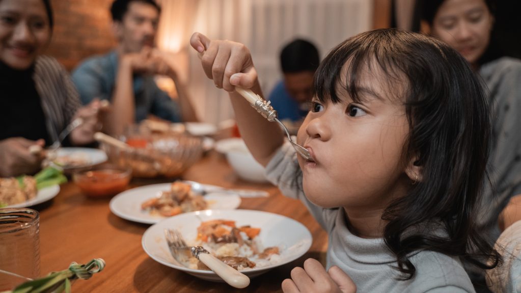 Girl eating from plate of food with family in background