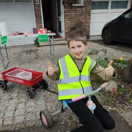 Boy in high vis sat on his trike selling baked goods for Felix