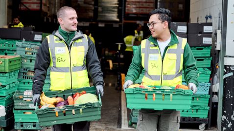 Two men in high vis walking towards camera with crates full of fruit and veg