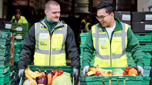 Two men in high vis walking towards camera with crates full of fruit and veg