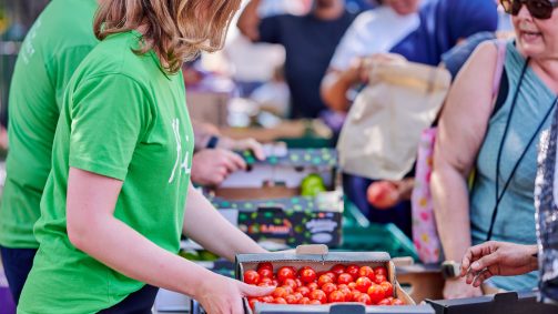 Woman in green holding cardboard box of tomatoes