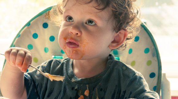 Toddler eating baked beans sat in a high chair