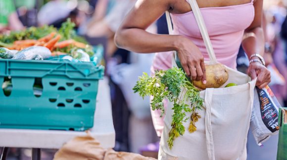 Woman in summery top placing vegetables into a plain tote bag