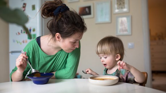 A woman and a young child sit together at the dining table with bowls of soup