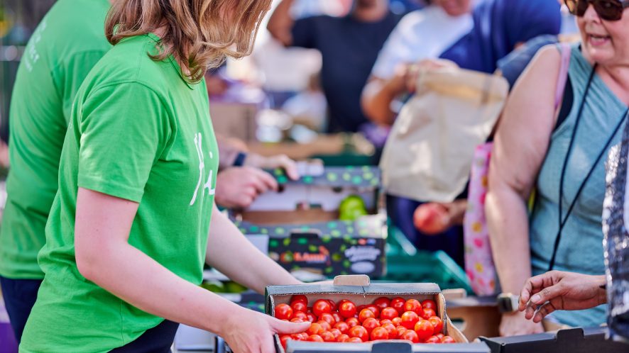 Woman in green holding cardboard box of tomatoes