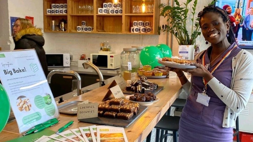 Woman standing next to bake sale holding plate of baked goods