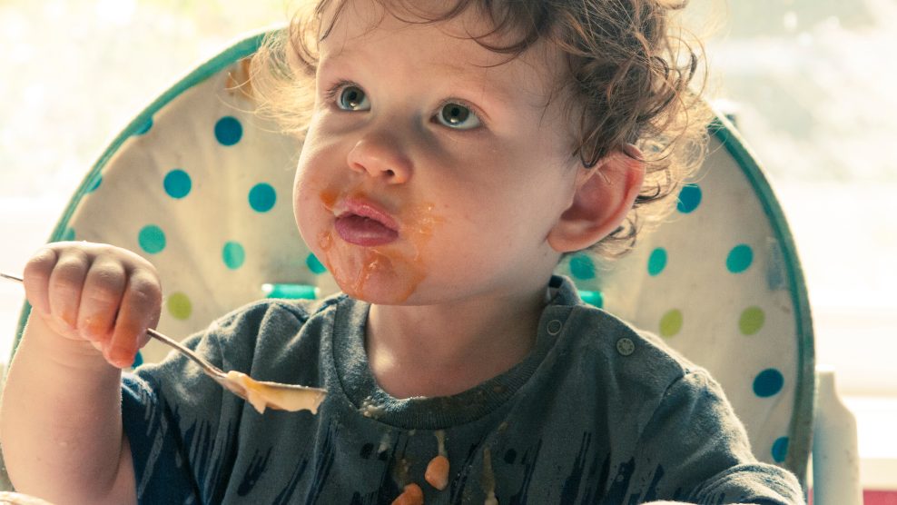 Toddler eating baked beans sat in a high chair