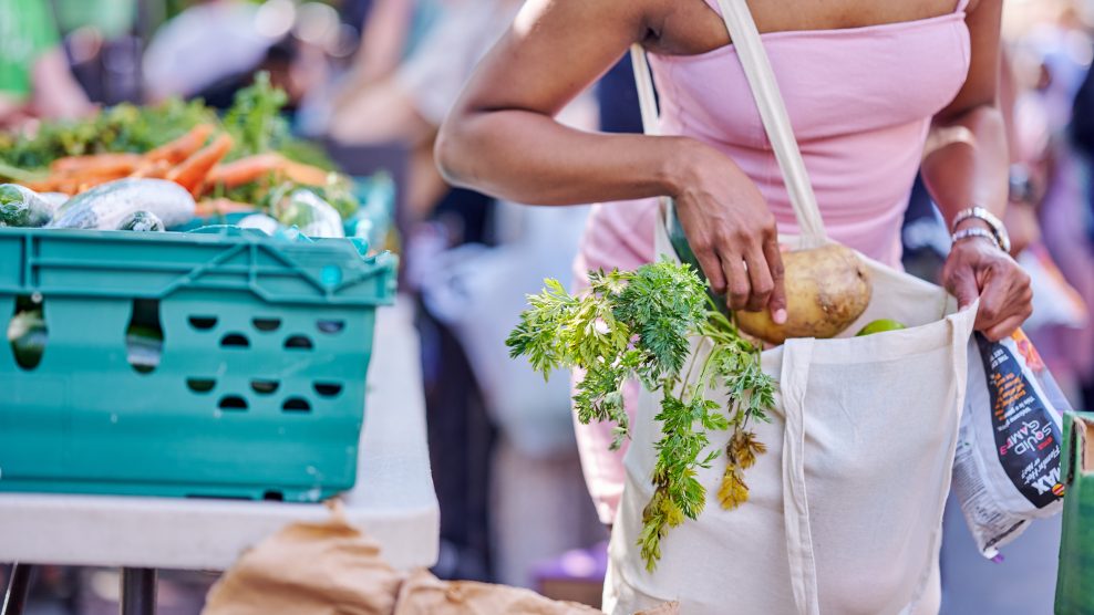 Woman in summery top placing vegetables into a plain tote bag