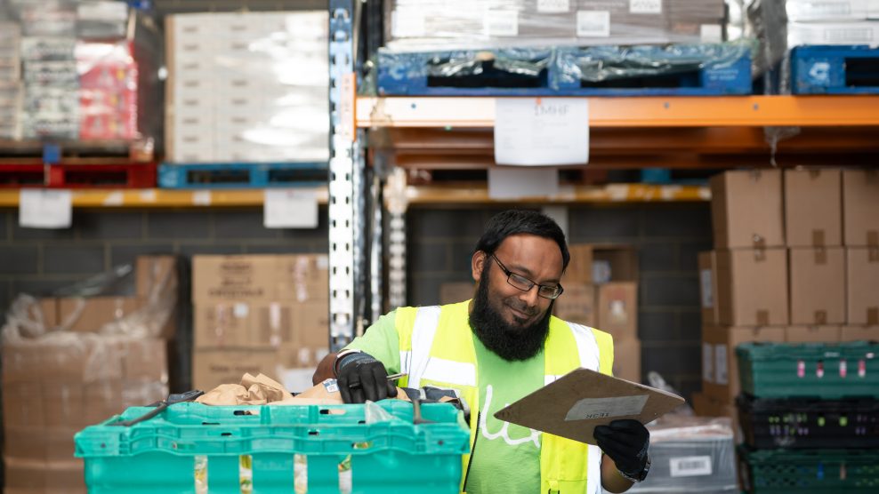 Man in high-vis looking at clipboard in a warehouse