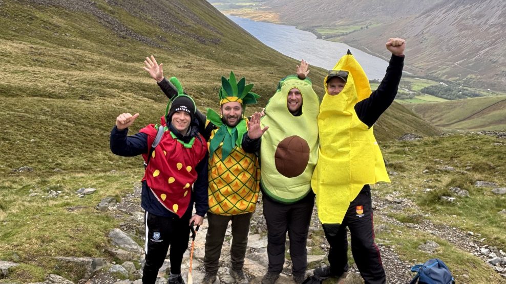 Four people at top of hill, wearing fruit costumes holding their hands in the air